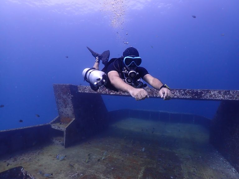 "PADI Instructor setting up sidemount harness with student before a shore dive"
