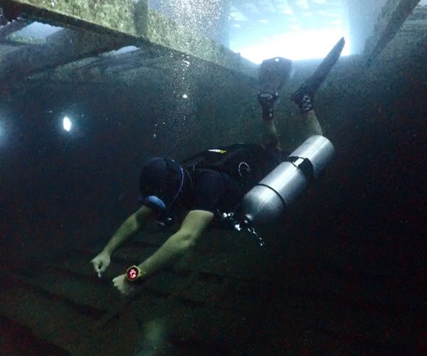 Wreck diver with flashlight looking inside cargo hold