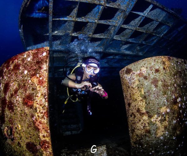 Diver hovering above a large propeller of a sunken ship