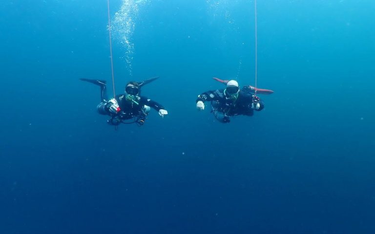 Two technical divers hovering mid-water while deploying surface marker buoys